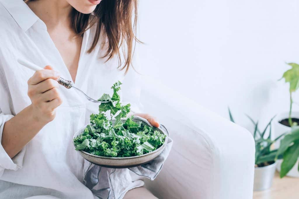 Mujer comiendo una saludable ensalada de col rizada.